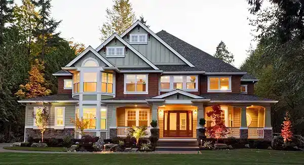 Two-story suburban house with large windows, front porch, and landscaped yard, illuminated by exterior lights at dusk—perfect inspiration for your house Plan Wishlist.