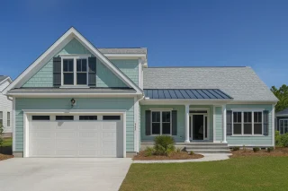 Front view of a Coastal Shingle style home with light blue horizontal and shingle siding, white trim, dark shutters, and a metal roof accent over the porch
